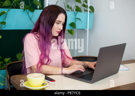 Giovane donna con capelli rosa con computer portatile in seduta cafe, intelligente studentessa lavorando su net-libro. Foto Stock