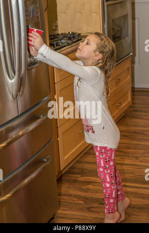 Bella bionda bambino, ottenendo un bicchiere di acqua dal frigo anteriore. Cranbrook BC, Canada. Modello rilasciato #113 Foto Stock