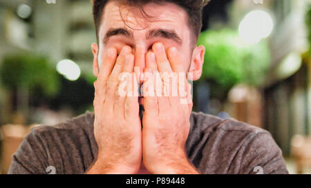 Giovane bello assonnato stanco uomo ubriaco con cocktail al di fuori di notte seduti al tavolo bar in una notte d'estate in città Foto Stock