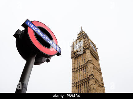 Guardare in su verso la stazione di Westminster e segno della metropolitana e il Big Ben di Londra contro un cielo chiaro prese con un obiettivo grandangolare Foto Stock