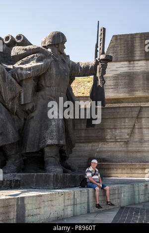 KIEV, UCRAINA - 9 agosto 2015: uomo seduto sotto una gigantesca statua comunista nel museo della Grande Guerra Patriottica, dedicato alla storia del Regno Unito Foto Stock