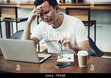 Asia casual uomo faccia del coperchio con lato sconvolto dal lavoro nella parte anteriore del computer portatile nella caffetteria,stress concetto emozione,lavoro fuori ufficio,lavoro a hom Foto Stock