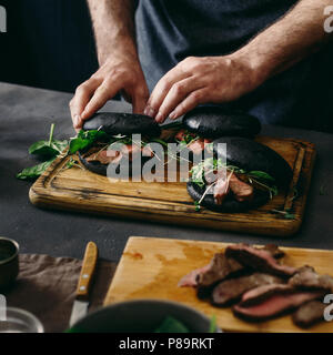 L'uomo nero Preparare hamburger con grigliate di carni bovine su sfondo scuro Foto Stock