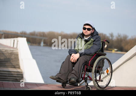 La Bielorussia, Gomel, 11 aprile 2018. Giornata della città. Central Park.Un uomo che indossa gli occhiali da sole in una sedia a rotelle per una passeggiata Foto Stock