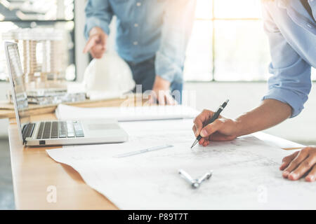 Close-up di persona ingegnere del disegno a mano sul piano di stampa blu con apparecchiature di architetto, architetti discutere al tavolo, il lavoro di squadra e il flusso di lavoro di co Foto Stock