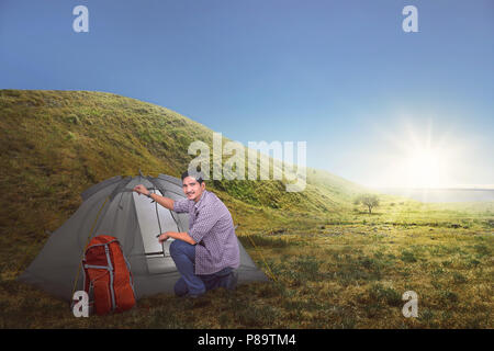 Attraente viaggiatori asiatici uomo impostare una tenda sul campo in erba Foto Stock