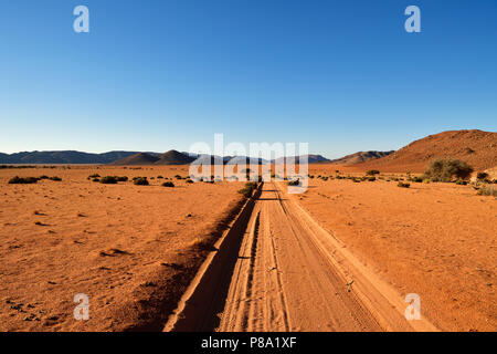 Sandtrack morbida in luce della sera conduce attraverso la steppa con monti all'orizzonte, Tiras mountains, Namibia Foto Stock