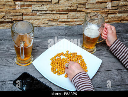 Una donna seduta in un bar, luce di bere birra e mangiare i dadi salata. Foto Stock