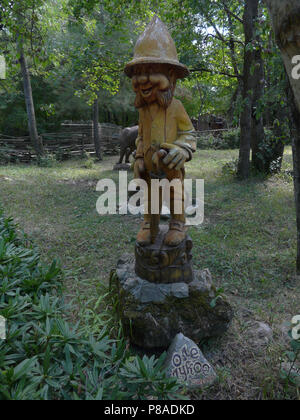 Una statua in legno di un gnome con un ombrello nelle sue mani si erge su una roccia nel parco . Per il vostro design Foto Stock