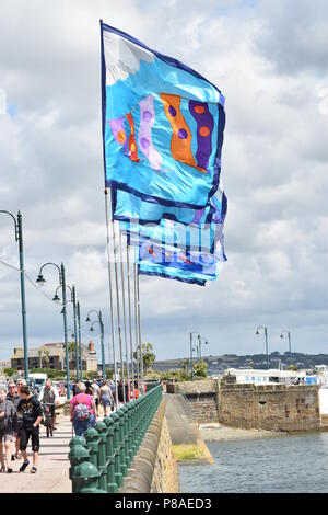 Multi bandiere colorate con pattern di inusuale in volo la brezza sul fronte mare di nubi in background a Penzance, Inghilterra Foto Stock