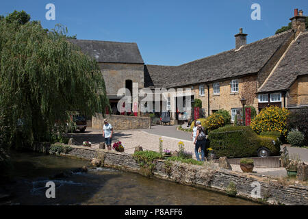 Bourton sull'acqua in Cotswolds, Regno Unito. Bourton-on-the-acqua è nota per le sue pittoresche High Street, fiancheggiata da lungo ampi green e il Fiume Windrush che scorre attraverso di esse. Il fiume è attraversato da più bassa, arcuata di ponti di pietra. Questi ponti ad arco hanno portato a Bourton-on-the-acqua che viene chiamata la "Venezia del Cotswolds'. Bourton-on-the-acqua spesso ha più visitatori che i residenti durante i periodi di picco della stagione turistica. I Cotswolds è una zona di South Central England. La zona è definita dalla roccia di calcare che si estrae per la dorata Cotswold Foto Stock