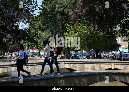 Bourton sull'acqua in Cotswolds, Regno Unito. Bourton-on-the-acqua è nota per le sue pittoresche High Street, fiancheggiata da lungo ampi green e il Fiume Windrush che scorre attraverso di esse. Il fiume è attraversato da più bassa, arcuata di ponti di pietra. Questi ponti ad arco hanno portato a Bourton-on-the-acqua che viene chiamata la "Venezia del Cotswolds'. Bourton-on-the-acqua spesso ha più visitatori che i residenti durante i periodi di picco della stagione turistica. I Cotswolds è una zona di South Central England. La zona è definita dalla roccia di calcare che si estrae per la dorata Cotswold Foto Stock