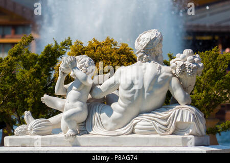 Scultura di gesso nella forma di un uomo sdraiato e ragazzo accanto a uno sfondo di cespugli e spruzzi di una fontana . Per il vostro design Foto Stock