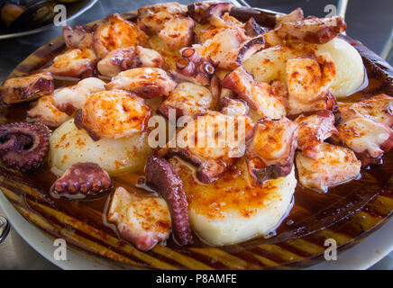 Polpo e patate cotte con paprica e olio d'oliva sulla piastra di legno. Il galiziano cibo Foto Stock