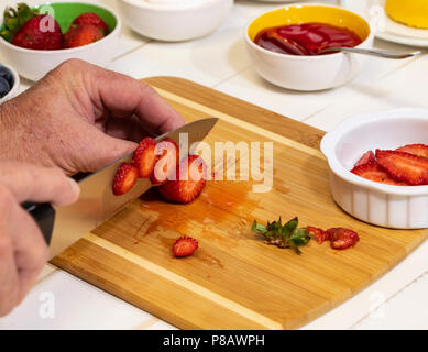 L uomo per affettare le fragole fresche su un tagliere. Foto Stock
