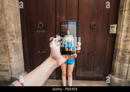 Crop mano azienda smartphone e prendendo la foto del giovane lady vicino dooron street di Valencia in Spagna Foto Stock