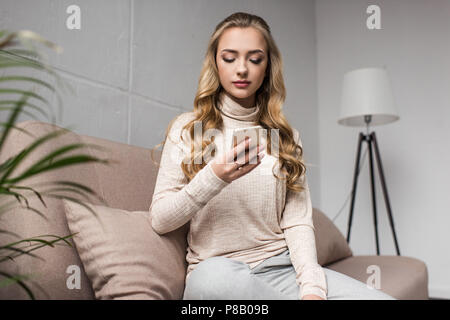 Bella giovane donna utilizza lo smartphone mentre Wittig sul lettino accogliente a casa Foto Stock