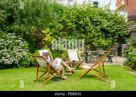 Vecchio uomo che indossa cappello di Panama risolvendo il cruciverba seduto nella sedia a sdraio nel giardino di grandi dimensioni in canicola estiva, London, England, Regno Unito Foto Stock