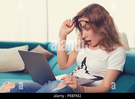 Giovani scioccato ansiosi donna guardando il computer portatile vedendo le cattive notizie foto email con paura emozione sul suo viso Foto Stock