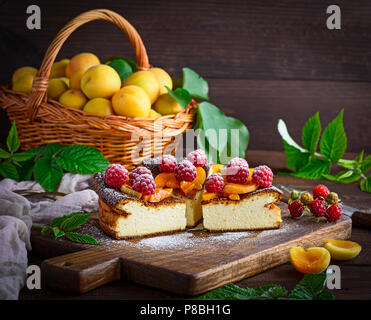 Torta di ricotta con lamponi e albicocche su un di legno marrone, scheda close up Foto Stock