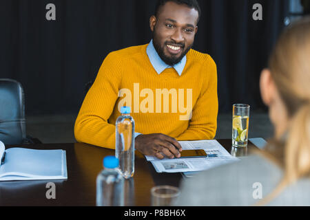Uomo d'affari multiculturali e imprenditrice guardando ogni altro a tavola in office Foto Stock