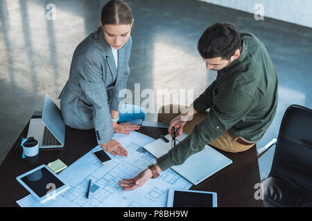 Elevato angolo di visione di imprenditore che mostra qualcosa a blueprint per imprenditrice Foto Stock