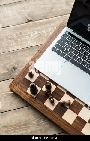 Scacchiera con pezzi di scacchi e portatile su rustico superficie in legno  Foto stock - Alamy