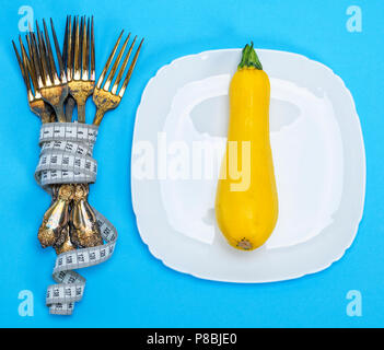 Zucca gialla su un piatto di portata in ceramica bianca, accanto a una pila di forche di ferro avvolto con nastro di misurazione, sfondo blu Foto Stock