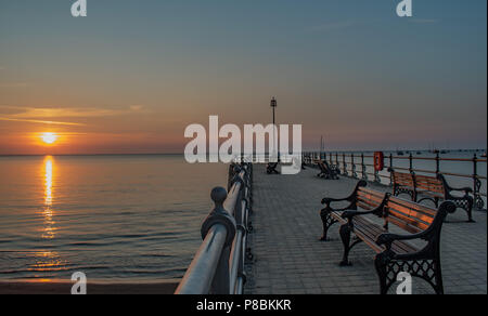 Un arancione incandescente Alba risplende attraverso il mare per raggiungere la riva a Swanage Foto Stock