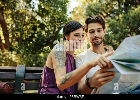 Turista giovane utilizzando una mappa per trovare il percorso verso la loro destinazione. L uomo e la donna i viaggiatori seduta su una panchina in un parco guardando una mappa. Foto Stock