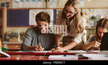 Ritratto di insegnante guardando il suo studente copybook spiegando gli errori. Docente aiutare lo studente durante la sua classe. Foto Stock