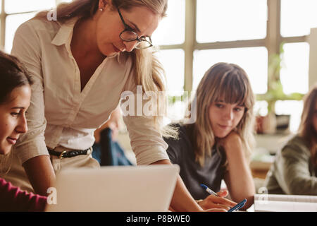 Insegnante di donna in piedi da una studentessa seduta in Aula. Docente femminile aiutando studente durante la sua classe. Foto Stock