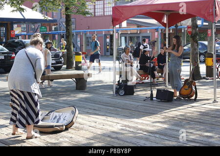 Un busker esegue a Granville Island e di un turista suggerimenti mentre lei lo esegue. Granville Island in Vancouver ha una reputazione per straordinarie prestazioni buksing. Foto Stock
