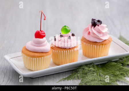 Rosa tortina con rosso ciliegia, mirtillo salse,verde jelly e cioccolatini su legno.Copia dello spazio. Foto Stock