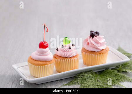 Rosa tortina con rosso ciliegia, mirtillo salse,verde jelly e cioccolatini su legno.Copia dello spazio. Foto Stock