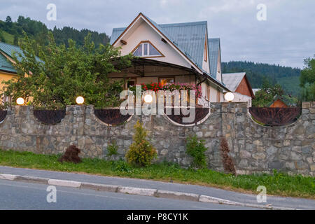 Una piccola bella recinzione di una casa privata con lanterne in cima. Con un tetto triangolare e verdi pendii visibile in distanza. . Per il vostro Foto Stock