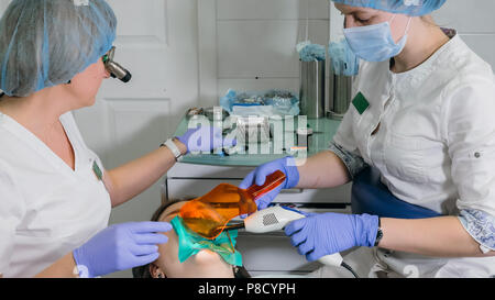 Donna al dentista clinica riceve il trattamento dentale per riempire una cavità di un dente. Restauro dentale e materiale composito la polimerizzazione con luce UV e laser. Foto Stock