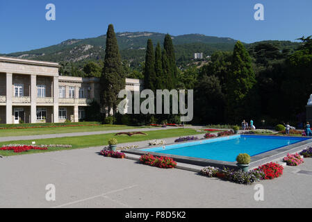 Piscina con acqua blu e letti di fiori sui lati nei pressi di un bellissimo edificio contro lo sfondo delle montagne verdi . Per il vostro design Foto Stock