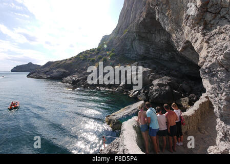 Una alta rupe presso la riva del mare sul quale la ragazza scende in acqua e la gente sta guardando per l. All'interno di rocce, la grotta è lavato Foto Stock