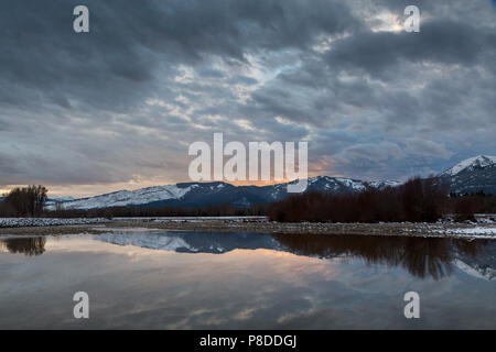Un nuvoloso tramonto riflesso in acque calme lungo il Fiume Snake. Emily Steven's Park, Wyoming Foto Stock