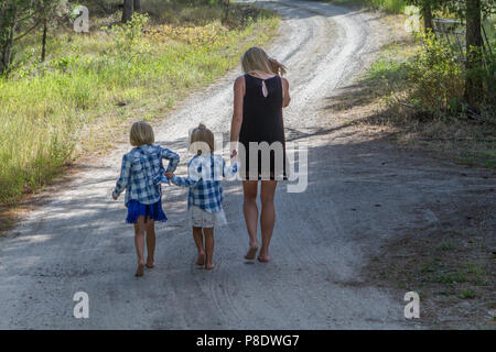 Umore foto di MOM e le figlie, tenendo le mani e a piedi lungo un paese strada sterrata. Modello rilasciato-dad #116, ragazza sulla sinistra #114 , ragazza sulla destra #11 Foto Stock