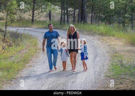 Attraente l uomo e la moglie, con i loro 4 e 6 anno vecchio figlie, camminando per un paese di strada sterrata, tenendo le mani, i piedi nudi. Modello rilasciato-dad #116, gi Foto Stock