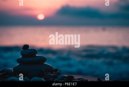 Piramide piegata Zen pietre ghiaia sul mare spiaggia al tramonto Foto Stock