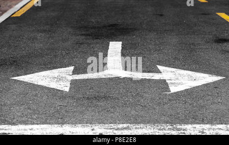 Solo gira a sinistra o a destra. Bianco freccia doppia, la segnaletica stradale su autostrada nero asfalto. Close-up foto con messa a fuoco selettiva Foto Stock