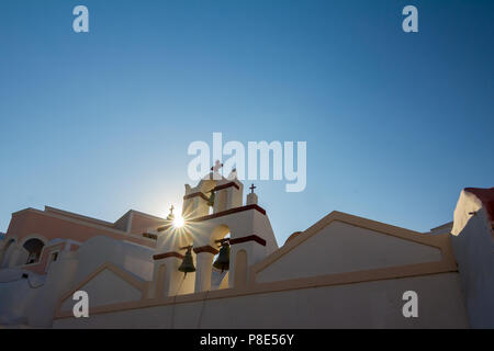 Romantico diffrazione Sun vicino Chiesa di Santorini. Fira, Grecia. Incredibile vista diurna verso le tre campane religiosa sulla parte superiore con Christia nero Foto Stock