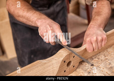 Chiusura del giovane uomo builder indossa in un plaid shirt il trattamento di un prodotto di legno con uno scalpello in officina, close-up Foto Stock