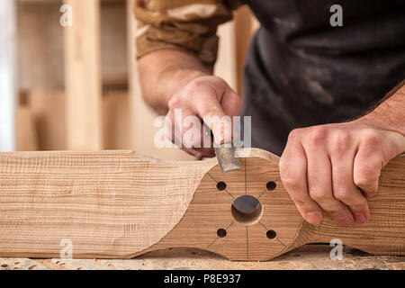 Chiusura del giovane uomo builder indossa in un plaid shirt il trattamento di un prodotto di legno con uno scalpello in officina, close-up Foto Stock