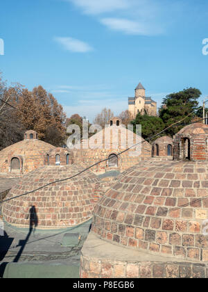 Vecchio a forma di cupola bathhouse tetti con Chiesa di Metekhi in background, Abanotubani distretto, Tbilisi, Georgia Foto Stock