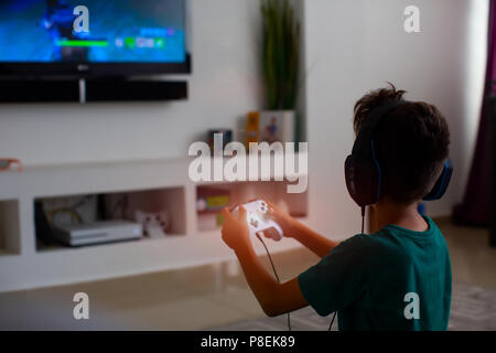 Video Gamer giocando un videogioco con joystick nelle sue mani- Un ragazzo da stupidi giochi online utilizzando la nuova tecnologia console su un grande schermo Foto Stock