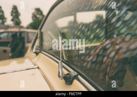 La riflessione del cielo nel parabrezza di un auto d'epoca contro lo sfondo di un salone con guanti di pelle sul volante Foto Stock